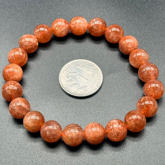 Beaded bracelet with orange beads and a coin for size comparison on a gray background