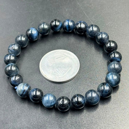 Blue Pietersite Bracelet with polished round beads arranged in a circle around a one rupee coin on a dark surface