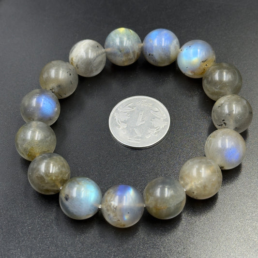 Labradorite Bracelet with round beads showing blue and yellow flashes around a small coin on dark surface