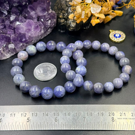 Two tanzanite certified bracelets with round beads next to a 1 rupee coin and ruler on black surface with amethyst crystal...