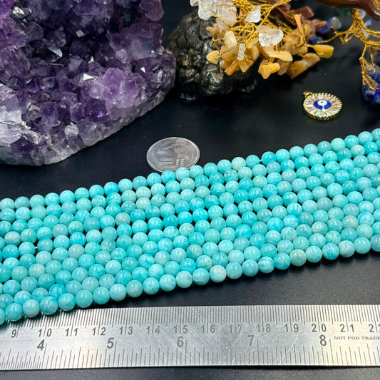 Multiple strands of round blue-green beads with a metal ruler and coin nearby, amethyst crystals, and a gold decorative ch...