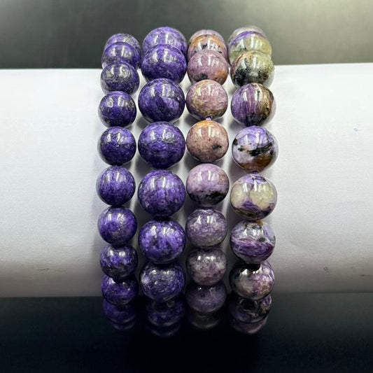 Charoite Bracelet with polished round beads in varying shades of purple and lavender tones on white display stand