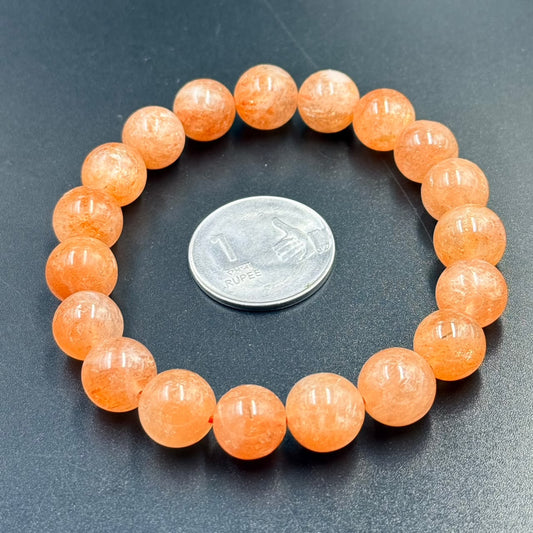 Sunstone Bracelet with round translucent orange beads arranged in a circle around a one rupee coin on a black surface