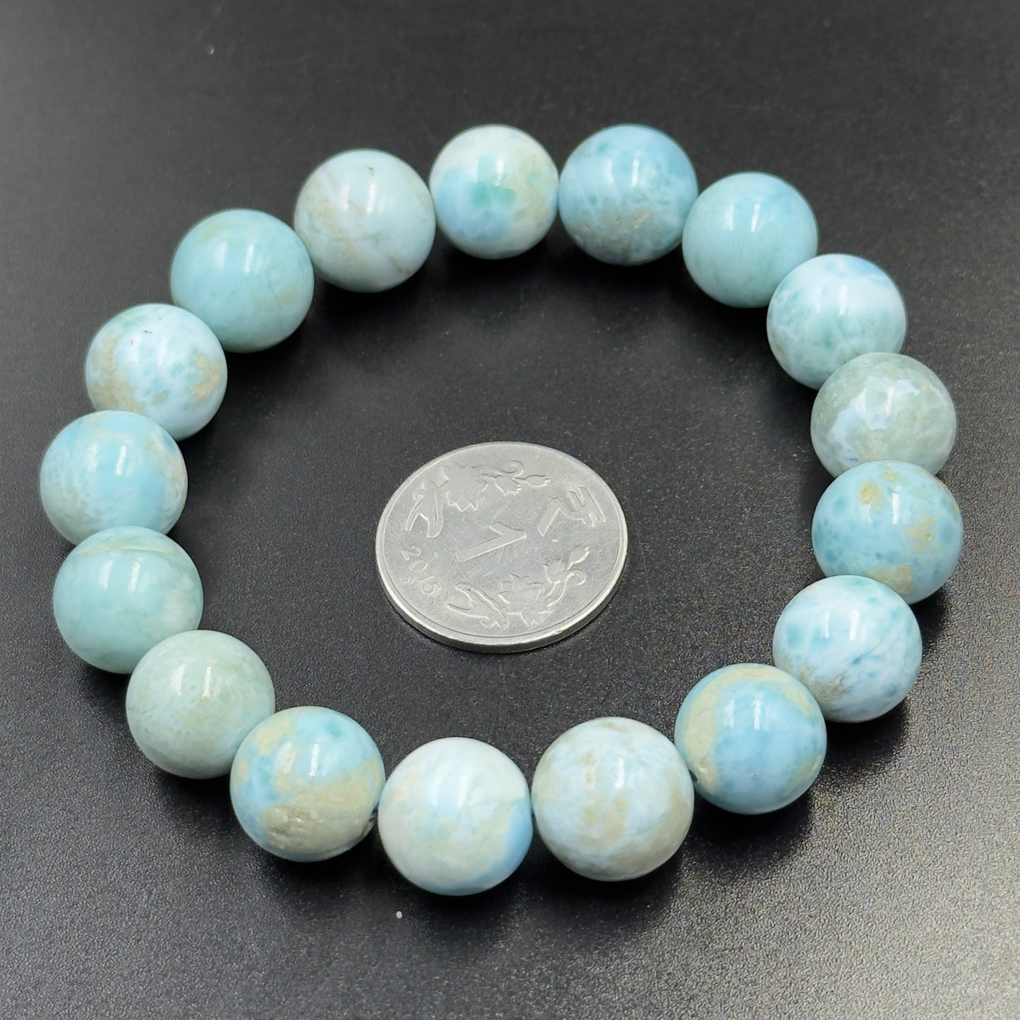 Larimar Bracelet with round light blue beads encircling a silver coin on a black background