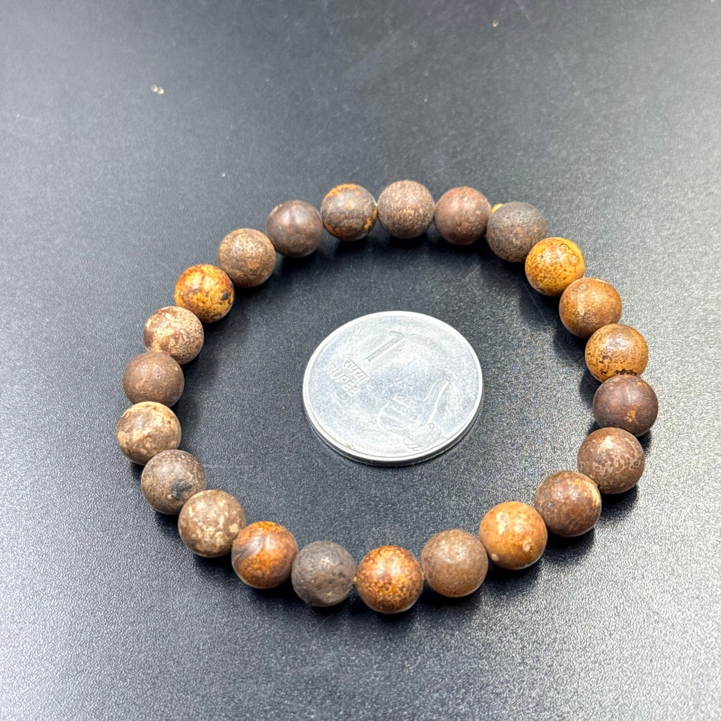 Bodhi Beads Bracelet for Peace laid flat beside a one rupee coin on a black surface