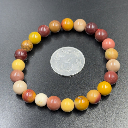 Australian Mookaite Bracelet Grounding Strength Stone with round multicolored beads and a coin on black background