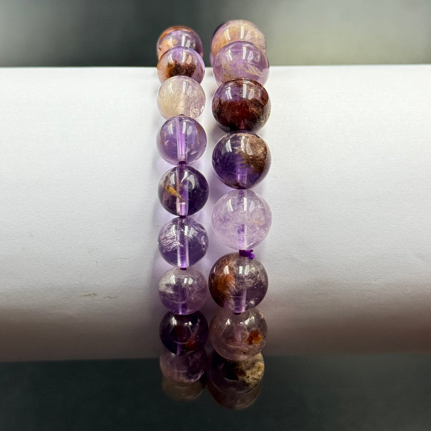 Two strands of round Ametrine Bracelet beads in varying shades of purple and amber on a white display stand