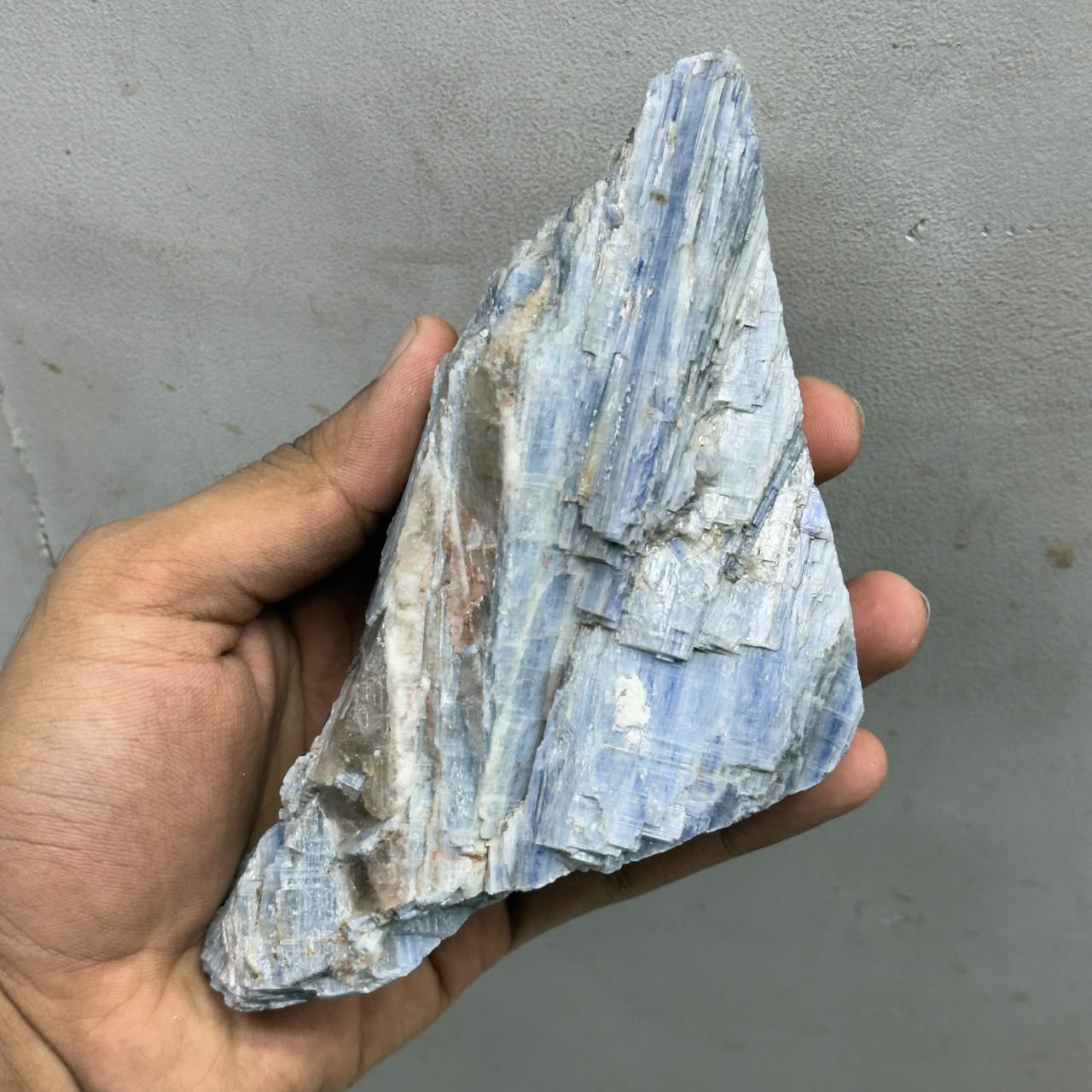 Natural rough blue kyanite gemstone specimen with vertical crystal blades held by hand