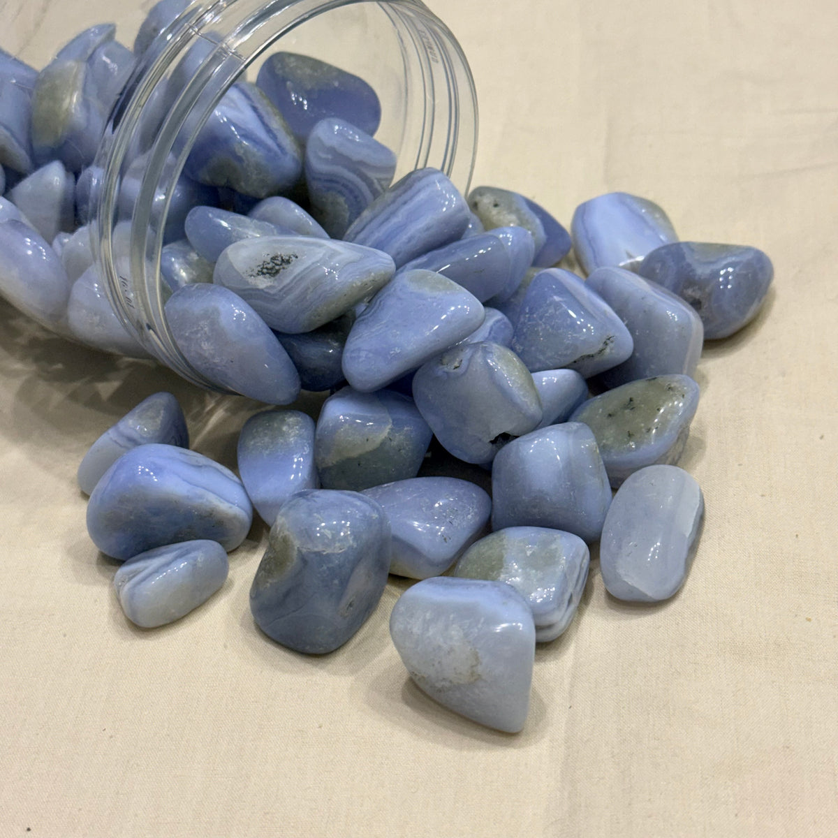 Blue lace agate tumble stones scattered in a glass jar, smooth polished stones