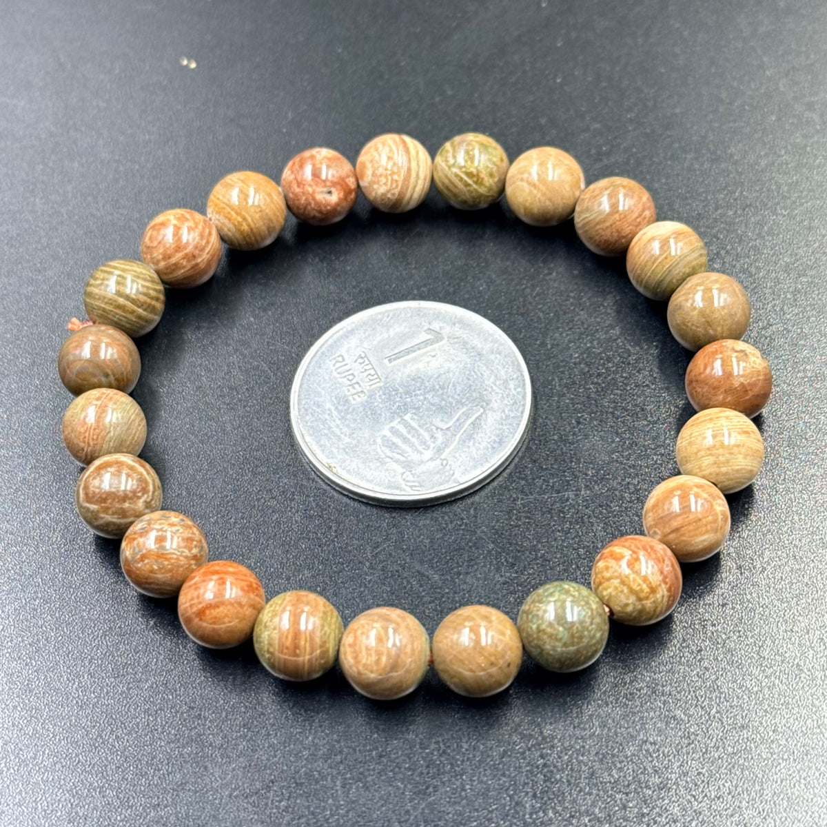 Color Cobble bracelet of round multicolor beads shown beside a large coin on dark fabric