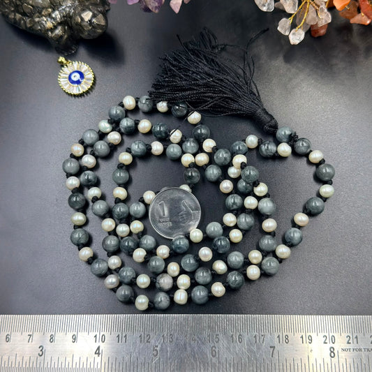 Cat’s Eye and Pearl Jaap Mala with black tassel, placed beside a coin and ruler on black surface