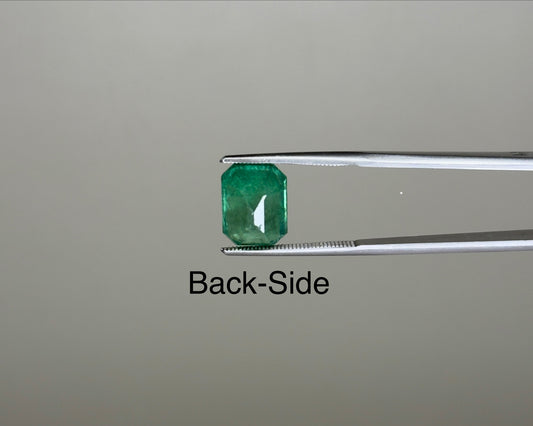 Back-side view of emerald green emerald-cut gemstone on tweezers