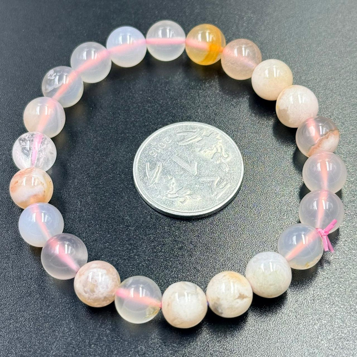 Flower agate bracelet beaded round design in pink, white, and honey tones on dark textured surface