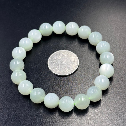 Green moonstone bead bracelet with round pale green beads beside a silver coin on dark fabric