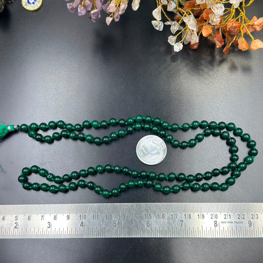 Green onyx jaap mala strands with tassel ends and coin for scale on dark background