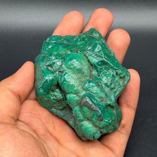 Natural rough malachite stone held in hand, textured green mineral surface