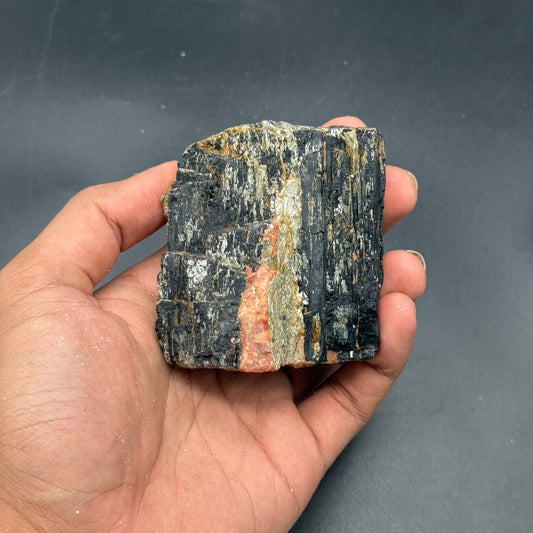Rough natural black tourmaline stone held in hand, dark crystal with orange streaks