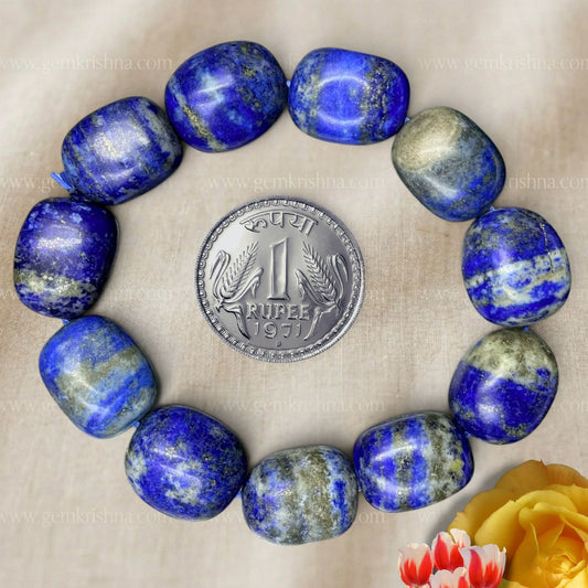 Lapis lazuli tumble bracelet laid in a circle with a coin for scale on beige fabric