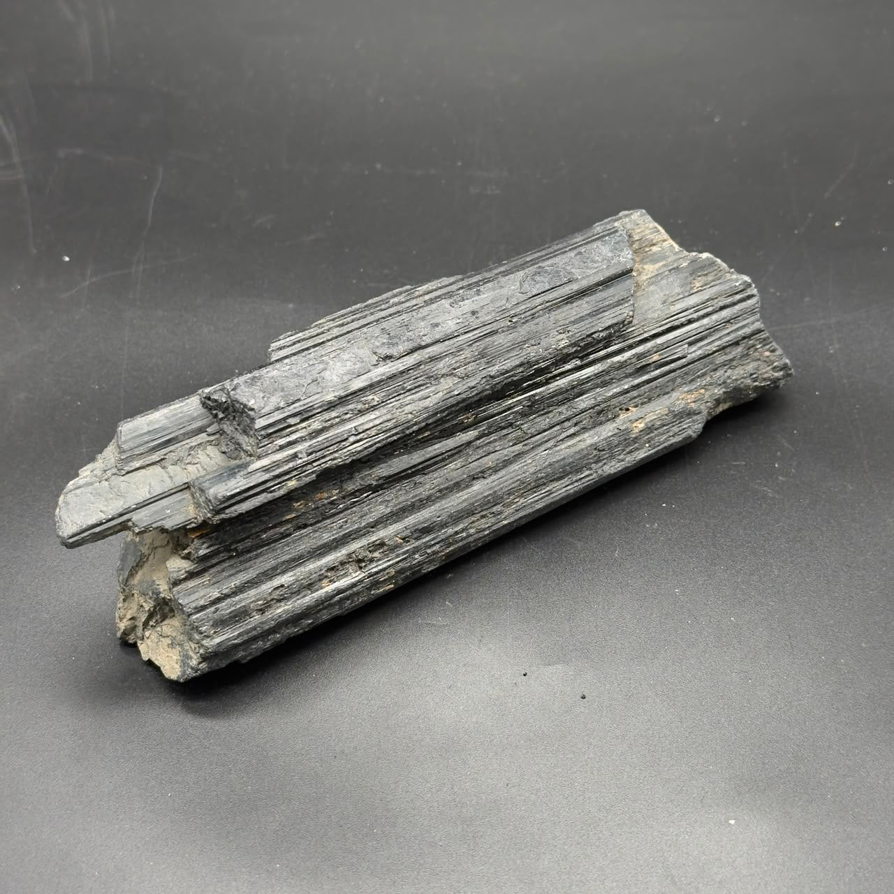 Large rough black tourmaline crystal showing parallel striations on a gray background