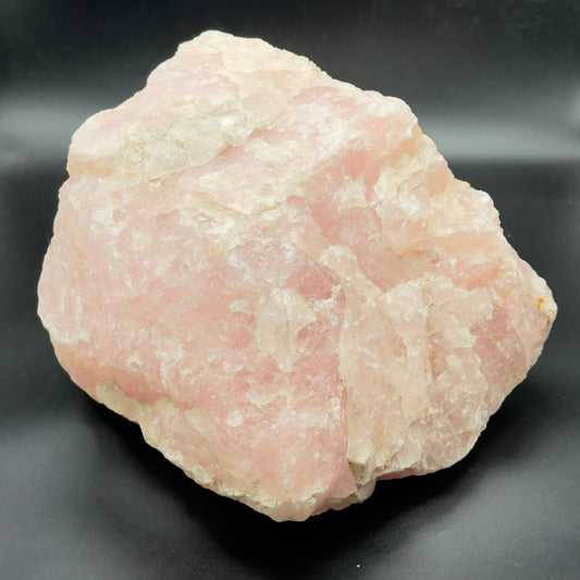 Large rough rose quartz crystal with pink and white crystal texture on dark surface