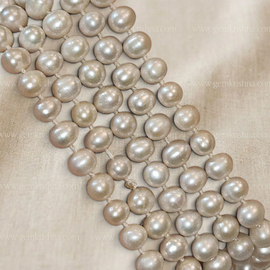 Loose line of round pearl beads with uniform cream shine laid on light fabric background