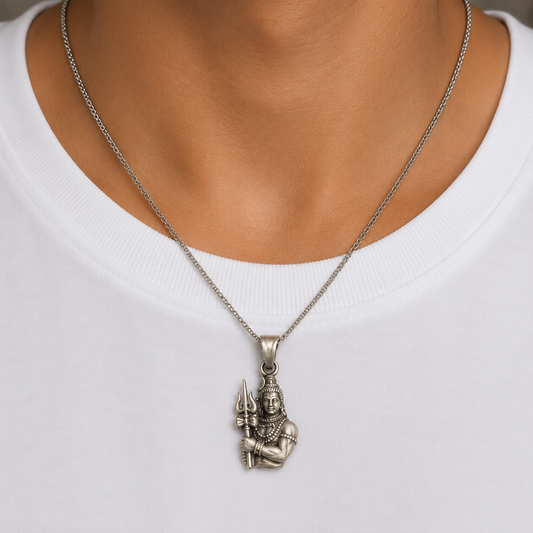 Lord Shiva trishul damru silver pendant worn on a chain against a white shirt