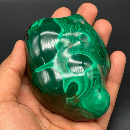 Polished freeform malachite stone held in hand showing glossy green banded patterns
