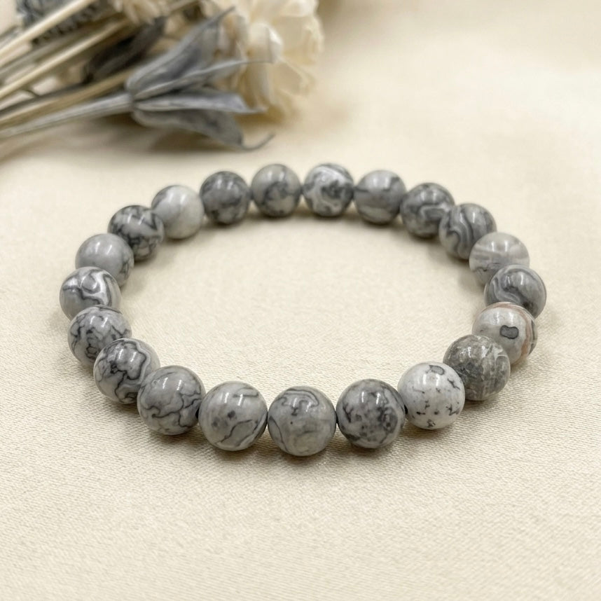 Mapstone bracelet with round gray and white marbled beads on a light cream surface