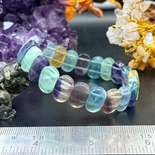 Multi fluorite flat oval bead bracelet with mixed colors on black display, ruler for scale