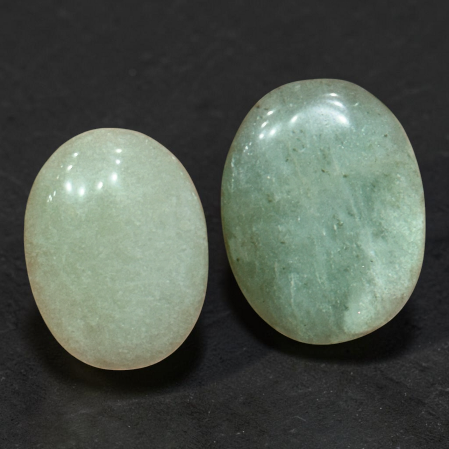 Natural green aventurine palm stones pair with glossy finish, shown side by side on dark fabric