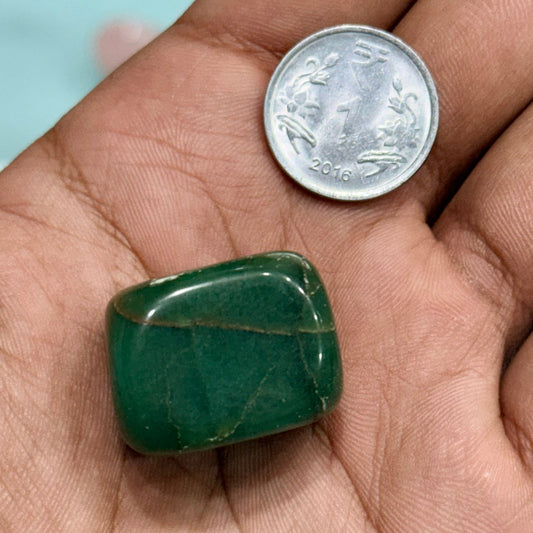 Natural green jade tumble stone beside a coin for size comparison
