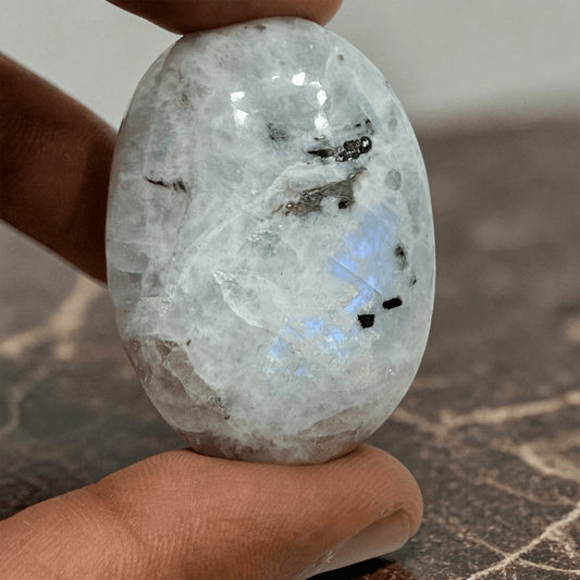Natural rainbow moonstone palmstone crystal held in hand close-up with blue sheen