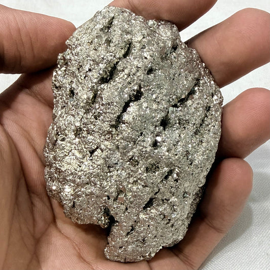 Natural raw pyrite crystal held in hands, showing rough metallic surface texture