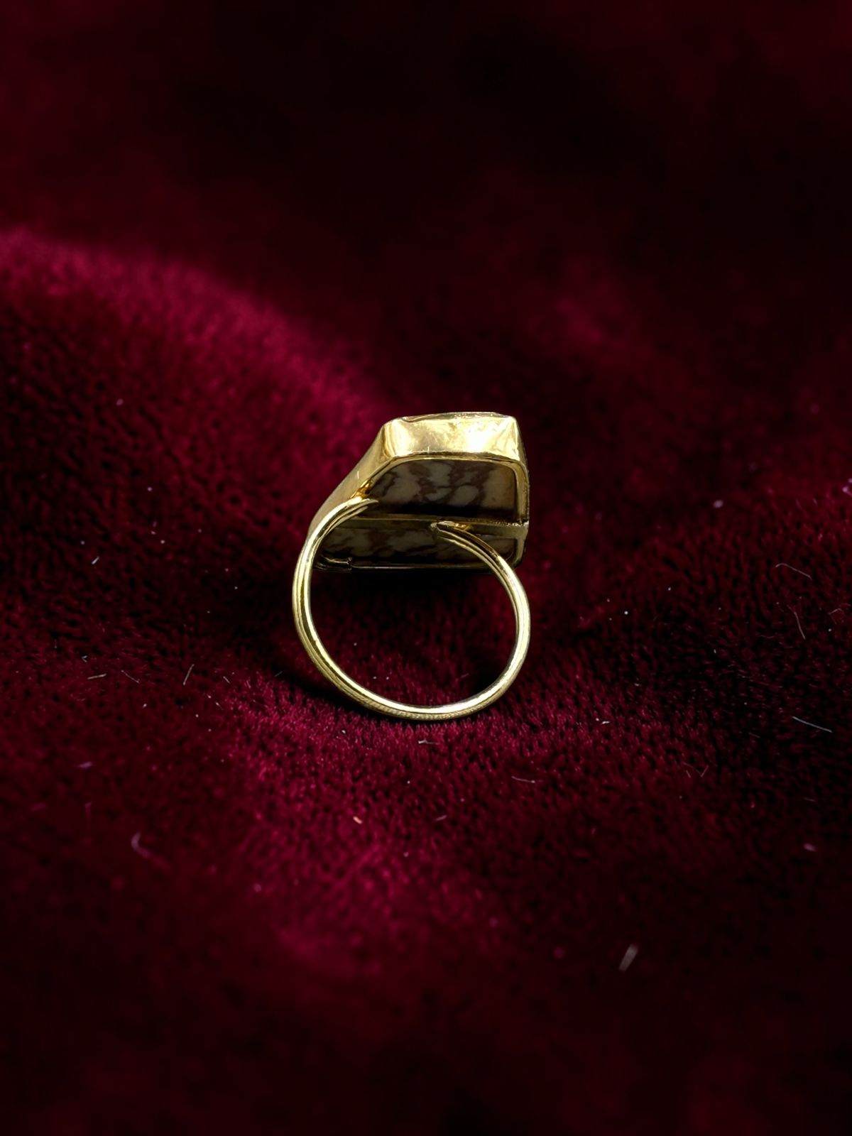 Back view of natural rhodonite rough stone metal ring on burgundy velvet