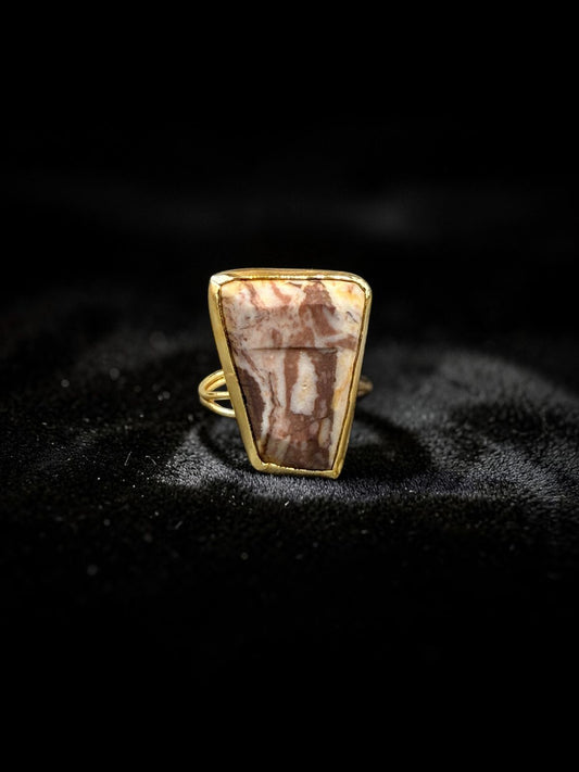 Natural rhodonite rough stone gold-tone metal ring on dark fabric background