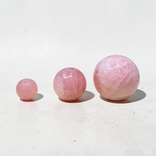 Natural rose quartz crystal ball spheres, glossy pink stones on light background studio set