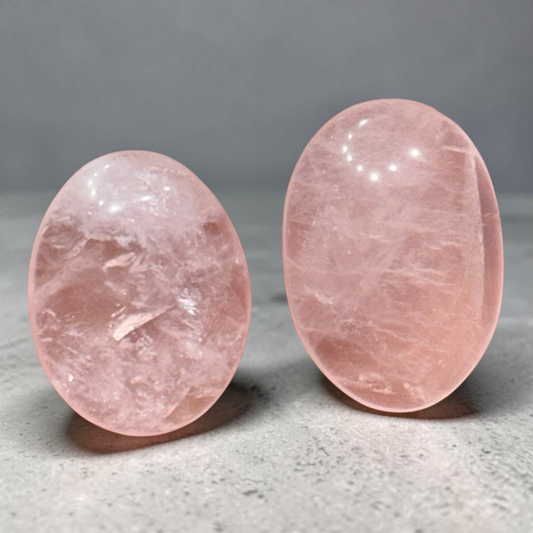 Natural rose quartz palm stone pair close-up on light gray textured background