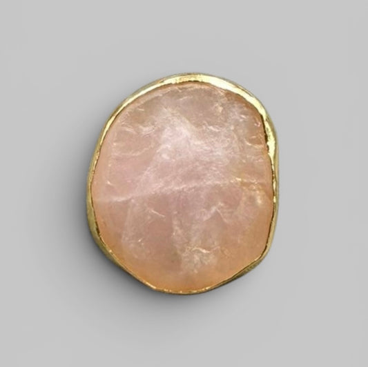 Natural rose quartz rough stone in gold-tone bezel setting on metal ring, close-up front view