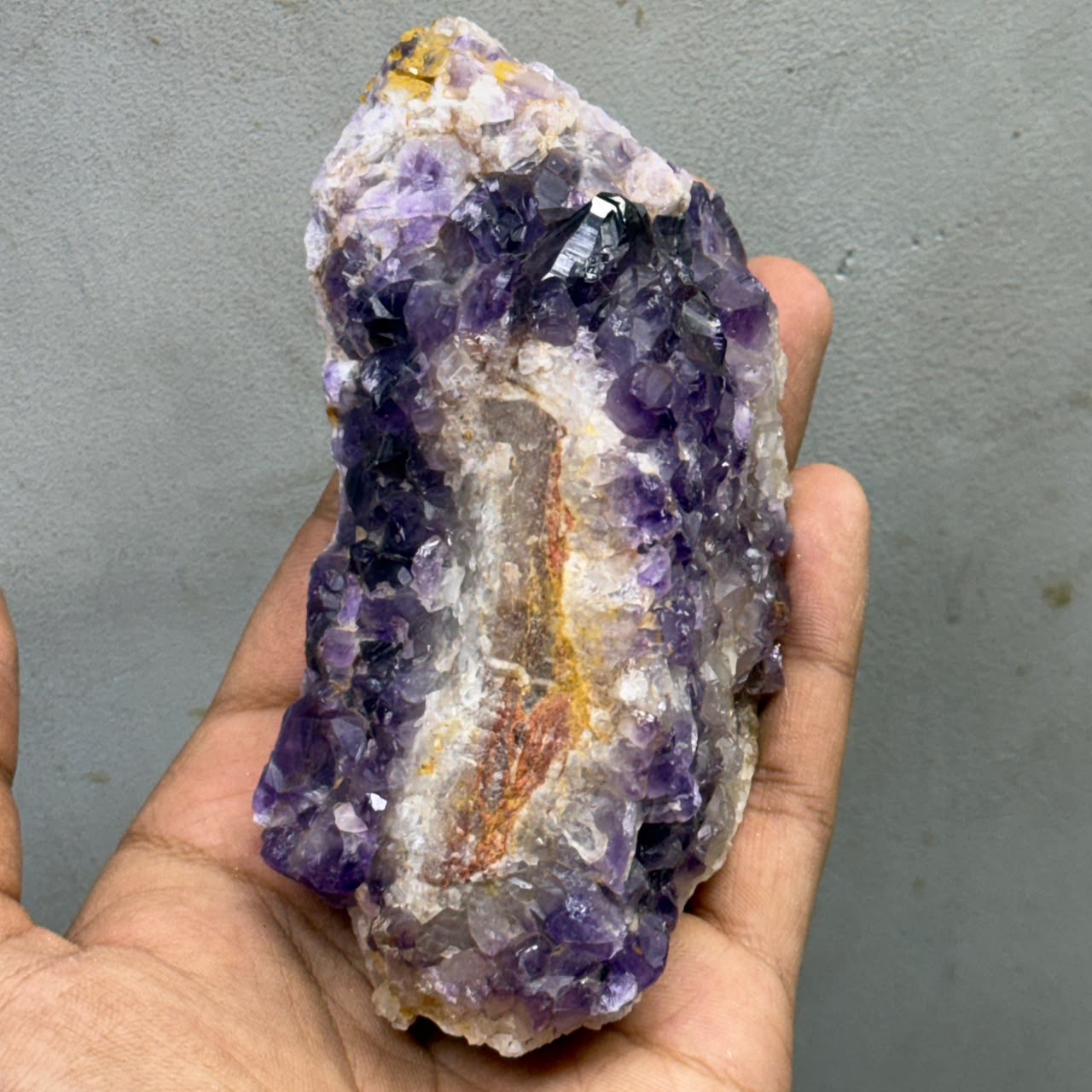 Natural rough amethyst crystal cluster held in hand, showing dense purple crystal points