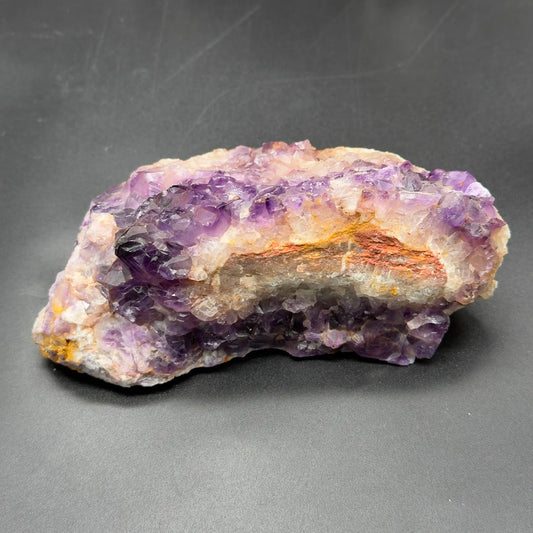 Natural rough amethyst crystal cluster on gray surface with purple crystals and light veining