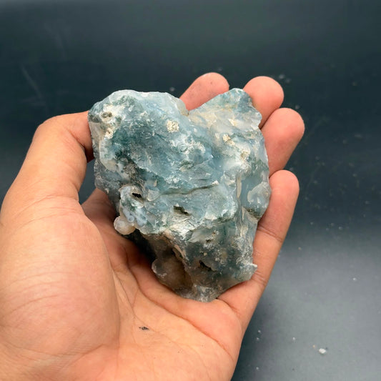 Natural rough moss agate crystal held in a hand, blue-green with light creamy matrix
