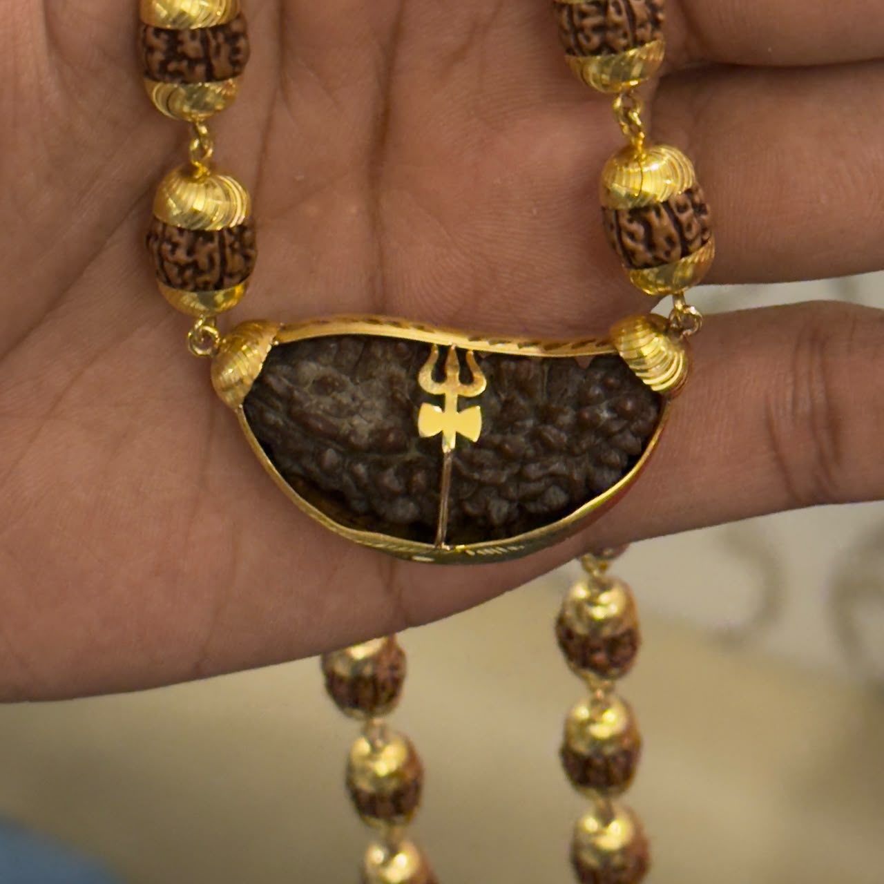 Close-up of gold-toned Om pendant and rudraksha beads on a gold-plated mala