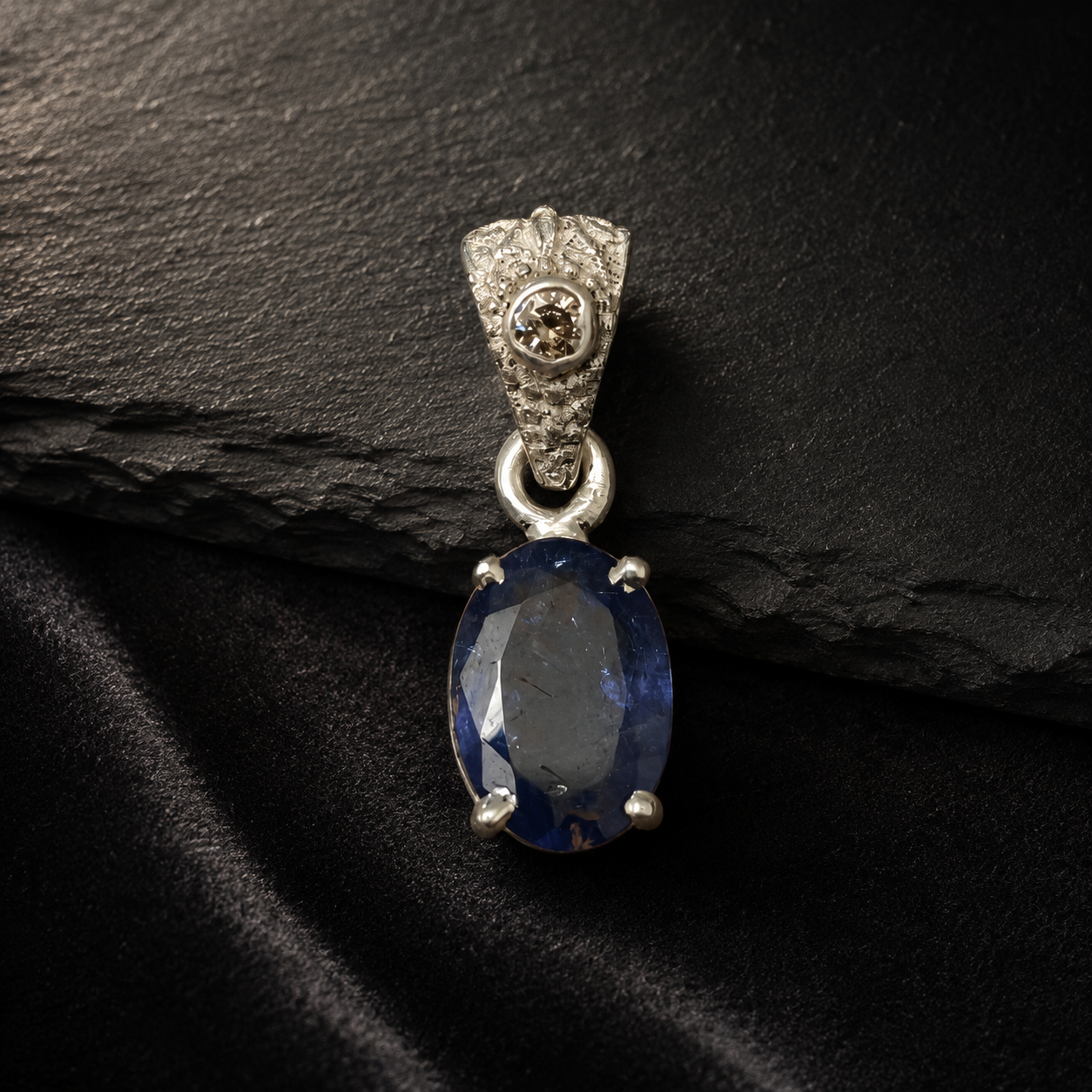 Oval blue tanzanite pendant with diamond-accented top in 925 silver on dark stone background