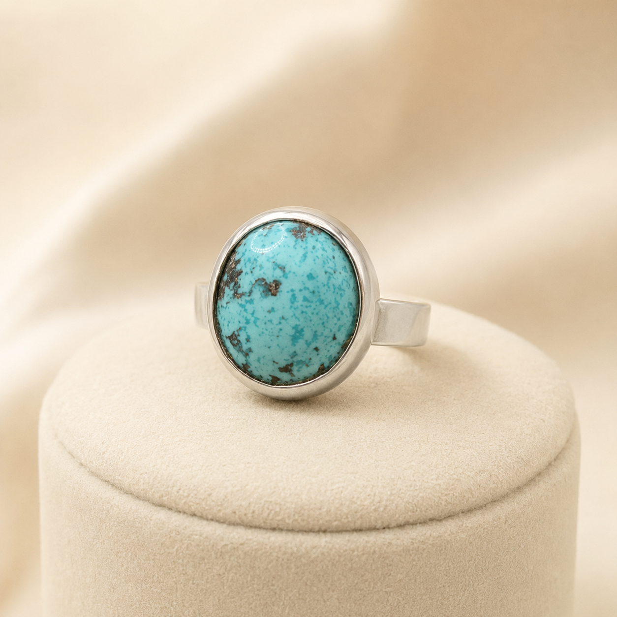 Side view of oval turquoise bezel ring with silver-toned band on beige cushion