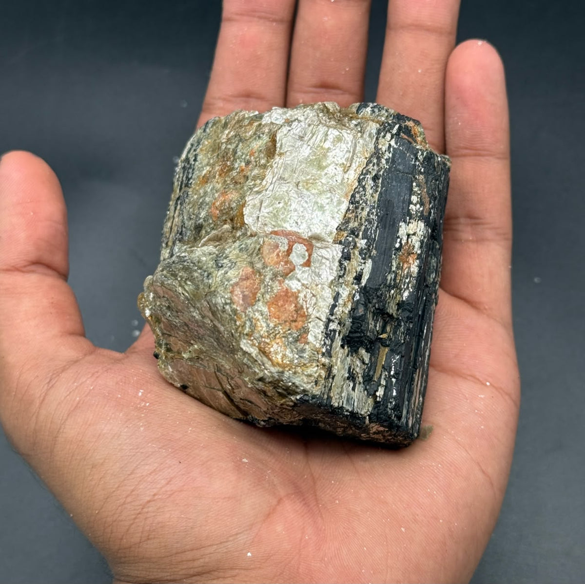 Natural rough black tourmaline crystal held in palm, textured dark stone with lighter patches