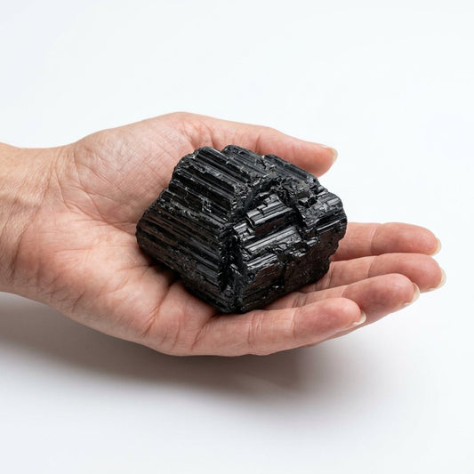 Raw black tourmaline crystal held in hand, natural dark prismatic surface on white