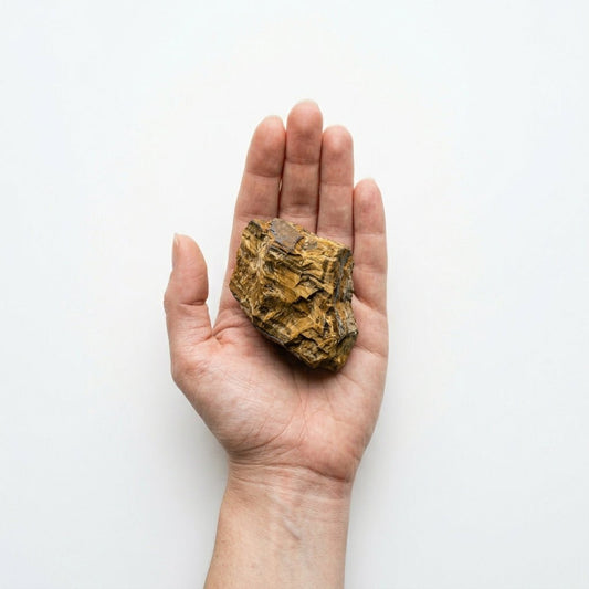 Raw tiger's eye crystal held in a hand for scale against a light background