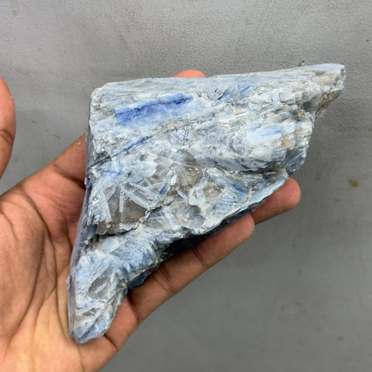 Natural rough blue kyanite specimen held in hand, showing crystal blade texture