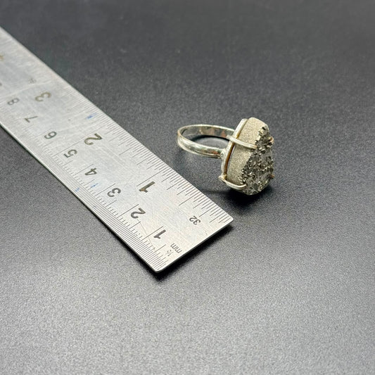 Rough pyrite stone ring shown beside a ruler for scale on dark tabletop background
