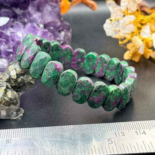 Ruby zoisite flat oval bead bracelet shown close up on dark surface with ruler for size
